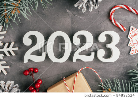 Happy New Year 2023. White numbers 2023 lying on gray uneven concrete surface with Christmas tree branches. Top view Happy New Year 2023. White numbers 2023 lying on gray uneven concrete surface with Christmas tree branches. Top view 94952524