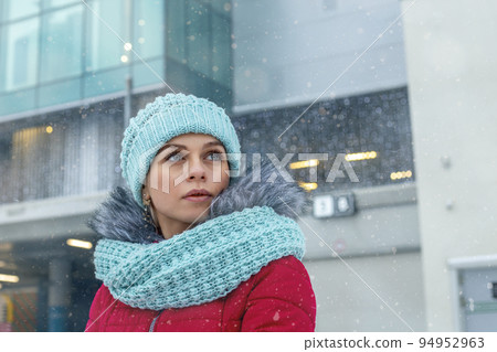 A young woman in a hat and scarf in a snowy city in winter. Looks forward to the future with hope. Close-up. A young woman in a hat and scarf in a snowy city in winter. Looks forward to the future with hope. Close-up. 94952963