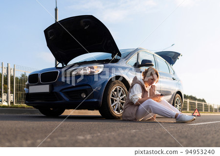 frustrated woman sitting on the road near the broken down car with the hood up, car insurance 94953240