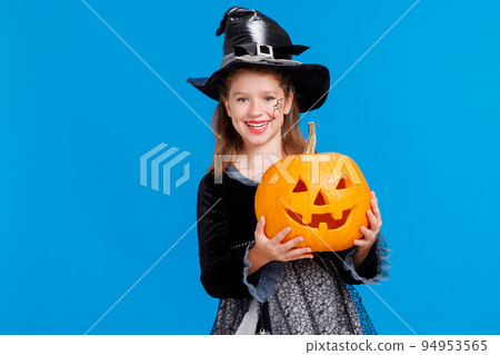Happy girl in witch costume with pumpkin jack-o-lantern celebrates Halloween and laughs on blue background 94953565