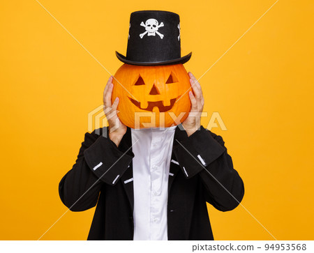 Happy man in a skeleton costume covers head with pumpkin and celebrates Halloween on yellow background 94953568