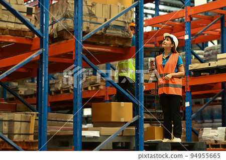 Warehouse workers wearing safety hardhat working on retail warehouse full of packed boxes and goods 94955665