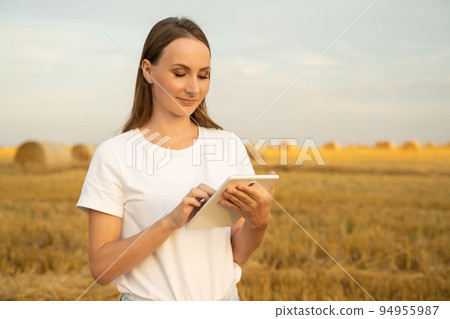 Female farmer stands in a wheat field at sunset and works with a digital tablet. Smart farming and precision farming Female farmer stands in a wheat field at sunset and works with a digital tablet. Smart farming and precision farming 94955987