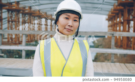 portrait of female builder standing outside construction area wearing safety helmet. People and technical profession concept. portrait of female builder standing outside construction area wearing safety helmet. People and technical profession concept. 94958080