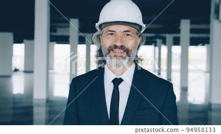 Portrait of successful real estate investor standing indoors in modern empty building wearing safety helmet and formal suit. People and occupation concept. 94958133