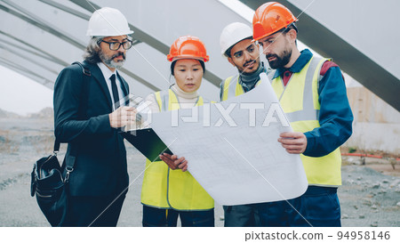 Construction workers are discussing project with manager standing in building area reading papers and looking around. People and occupation concept. Construction workers are discussing project with manager standing in building area reading papers and looking around. People and occupation concept. 94958146