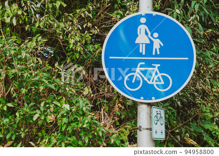 German Sign Sidewalk With Bike Path. Blue Background With Pedestrian And Bicycle. Dutch Blue Traffic Sign With Green Leaves. Road Sign Path For Bicycles And Walks With Children German Sign Sidewalk With Bike Path. Blue Background With Pedestrian And Bicycle. Dutch Blue Traffic Sign With Green Leaves. Road Sign Path For Bicycles And Walks With Children 94958800