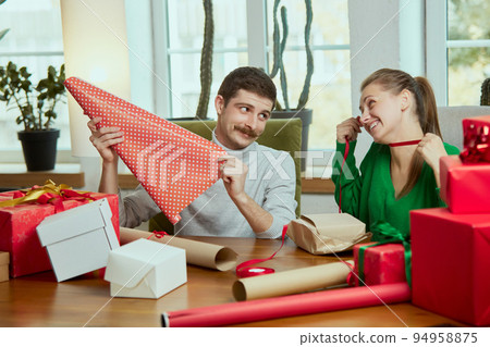 Portrait of cute young people, man and woman wrapping christmas presents together at home, making holiday preparations Portrait of cute young people, man and woman wrapping christmas presents together at home, making holiday preparations 94958875