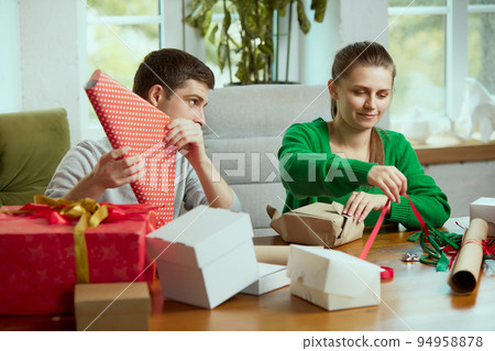 Portrait of cute young people, man and woman wrapping christmas presents together at home, making holiday preparations 94958878