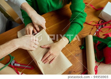 Top view image of man and woman wrapping presents together at home, using wrapping paper and ribbons. 94958903