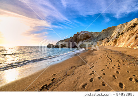 Low sun over beach, cliffs and hills and deep azure sea. Agios Ioannis beach, Milos island, Greece. Low sun over beach, cliffs and hills and deep azure sea. Agios Ioannis beach, Milos island, Greece. 94958993