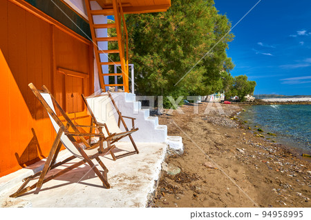 Two beach chairs on porch of traditional fisherman house by seafront. Summer sunshine, sunny day, perfect vacation location, getaway. Two beach chairs on porch of traditional fisherman house by seafront. Summer sunshine, sunny day, perfect vacation location, getaway. 94958995
