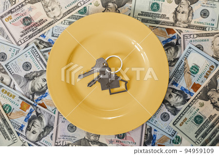 A yellow plate with keys with a keychain in the form of a house on the background of scattered American dollar bills. Flat lay. Concept of leasing, rental and purchase of real estate A yellow plate with keys with a keychain in the form of a house on the background of scattered American dollar bills. Flat lay. Concept of leasing, rental and purchase of real estate 94959109