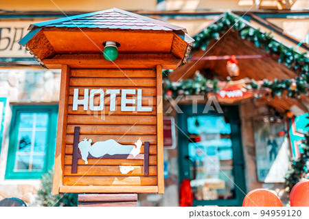 Wooden vintage decorative sign with the inscription hotel, and the image of a sleeping person. In the background the entrance to the hotel in a blur. Concept of hotel business and travel Wooden vintage decorative sign with the inscription hotel, and the image of a sleeping person. In the background the entrance to the hotel in a blur. Concept of hotel business and travel 94959120