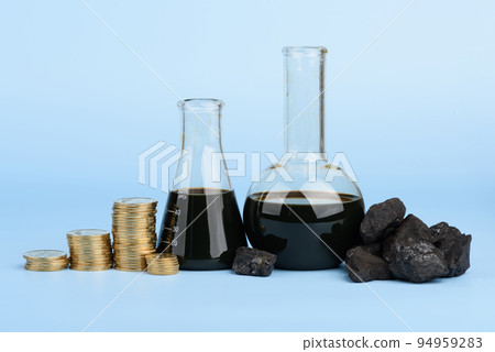 Crude oil in glass beakers and black hard coal lumps with coins stacks on blue background 94959283