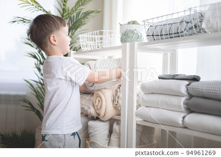 The child puts the bedding in a closet with neatly folded things. vertical storage. The child puts the bedding in a closet with neatly folded things. vertical storage. 94961269