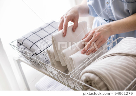 Modern housewife putting neatly folded towels, pillowcases, duvet covers into plastic metallic case 94961279