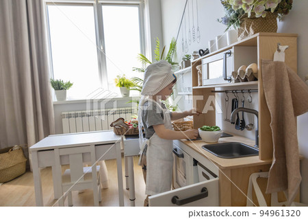 Cute little baby boy in chef hat and apron playing at childish kitchen cooking food back view 94961320