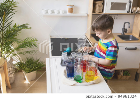 Cute baby boy learning mixing different colors with water and paint in containers. Early development 94961324