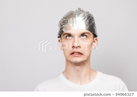 Paranoid young man wearing tin foil hat studio shot on gray background 94966327