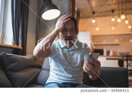 Mature man spending time at home and watching something on his smartphone 94966453