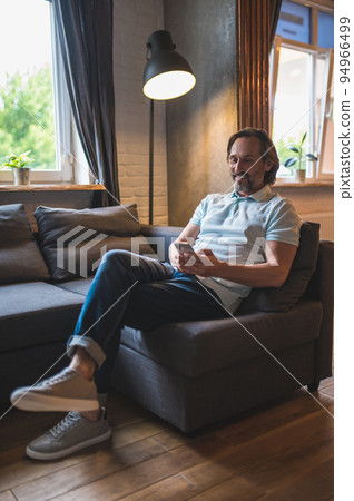 Bearded man sitting in the armchair awith a smartphone in hand Bearded man sitting in the armchair awith a smartphone in hand 94966499