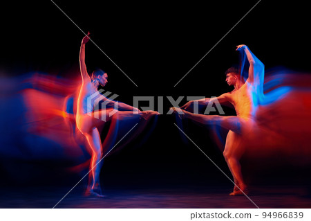 Confrontation between two. Couple of graceful and fragile ballet dancers in action isolated over black background in mixed neon light. Futurism, fantasy, miracle. 94966839