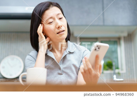 A woman holding a smartphone with a tired expression 94968360