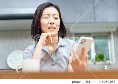 A woman holding a smartphone with a tired expression A woman holding a smartphone with a tired expression 94968361