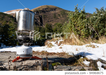 Preparing food for trips. Kettle on a gas stove. Kettle on the background of the mountains. Preparation of coffee. 94968675