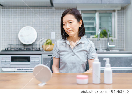 A middle-aged woman checking her skin condition with an uneasy expression 94968730