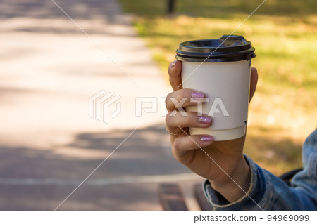 Hand holding coffee to go cup. Take away drinks. Girl holding coffee takeaway in park. City lifestyle. Coffee break in park. Street life concept. Hot drink in paper cup with copy space. Hand holding coffee to go cup. Take away drinks. Girl holding coffee takeaway in park. City lifestyle. Coffee break in park. Street life concept. Hot drink in paper cup with copy space. 94969099
