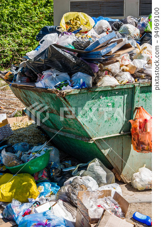 Overfilled trash dumpster in ghetto neigborhood. Trash container surrounded by heaps of garbage Overfilled trash dumpster in ghetto neigborhood. Trash container surrounded by heaps of garbage 94969100