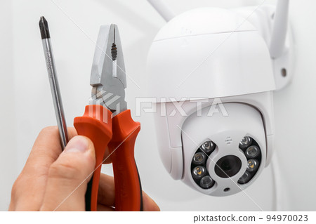 Technician installing CCTV camera using pliers and screwdriver outside of the building. 94970023