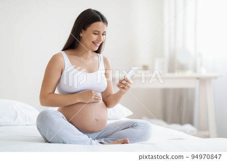 Happy expecting lady using smartphone, bedroom interior Happy expecting lady using smartphone, bedroom interior 94970847