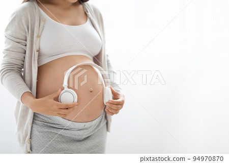 Cropped of expecting lady holding headphones on her big belly Cropped of expecting lady holding headphones on her big belly 94970870