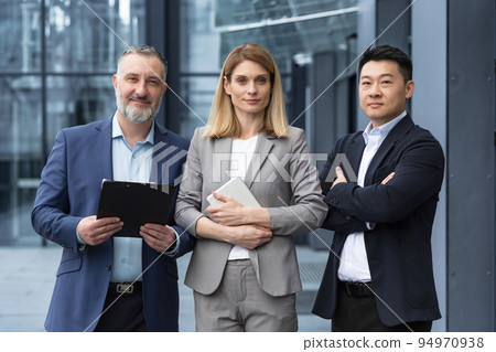 Diverse team man and woman outside office building business people with crossed arms looking thoughtfully at camera colleagues employees three persons 94970938