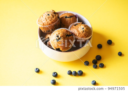 Blueberry muffins served in a bowl on a yellow background. Overhead view. Blueberry muffins served in a bowl on a yellow background. Overhead view. 94971505