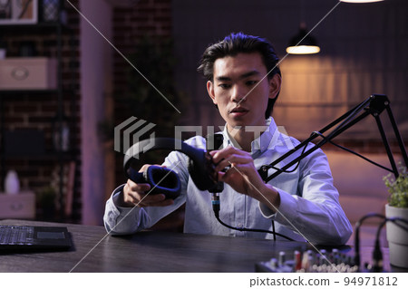 Male vlogger reviewing headphones on livestream, filming podcast video with headset product recommendation. Recording online vlog with sound station and creating social media content. 94971812