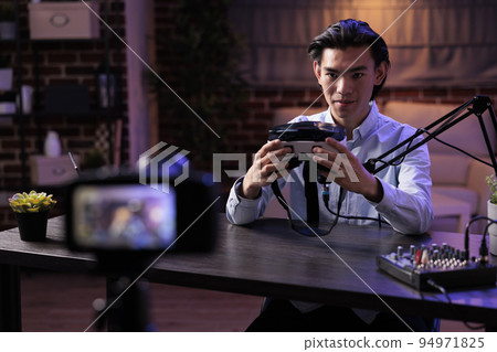 Asian freelancer livestreaming product review on internet channel, filming vr glasses recommendation with podcast equipment at sound station. Recording online video with virtual reality goggles. Asian freelancer livestreaming product review on internet channel, filming vr glasses recommendation with podcast equipment at sound station. Recording online video with virtual reality goggles. 94971825