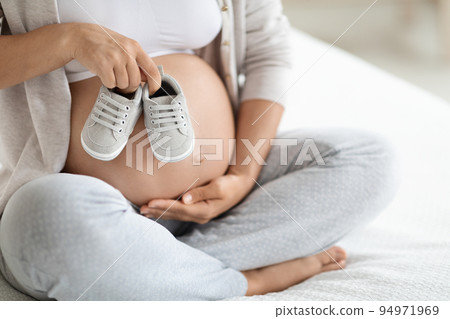 Cropped of pregnant woman holding baby shoes on big tummy 94971969