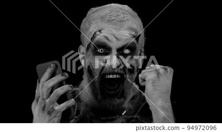 Happy excited sinister man Halloween zombie use smartphone celebrating lottery win, success luck Happy excited sinister man Halloween zombie use smartphone celebrating lottery win, success luck 94972096