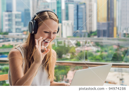 Young woman teaches a foreign language or learns a foreign language on the Internet on her balcony against the backdrop of a big city. Online language school lifestyle 94974286