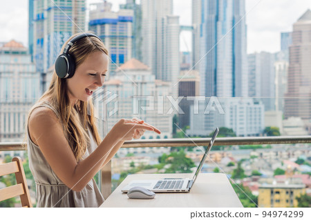 Young woman teaches a foreign language or learns a foreign language on the Internet on her balcony against the backdrop of a big city. Online language school lifestyle 94974299