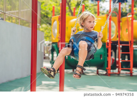 Funny kid boy having fun with chain swing on outdoor playground. child swinging on warm day. Active leisure with kids. Boy wearing casual colorful school kid clothes Funny kid boy having fun with chain swing on outdoor playground. child swinging on warm day. Active leisure with kids. Boy wearing casual colorful school kid clothes 94974358