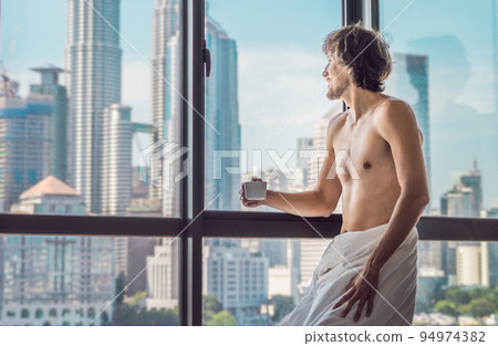 Man wakes up in the morning in an apartment in the downtown area with a view of the skyscrapers and drinks coffee. Life in the noise of the big city concept. Not enough sleep 94974382