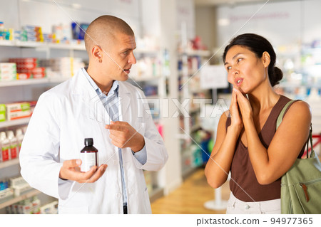 Woman with toothache asks the pharmacist what medicine to buy Woman with toothache asks the pharmacist what medicine to buy 94977365