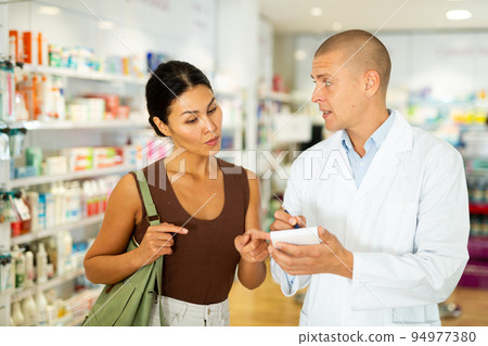 Pharmacist writes in notebook name of the drugs that the buyer tells him to Pharmacist writes in notebook name of the drugs that the buyer tells him to 94977380