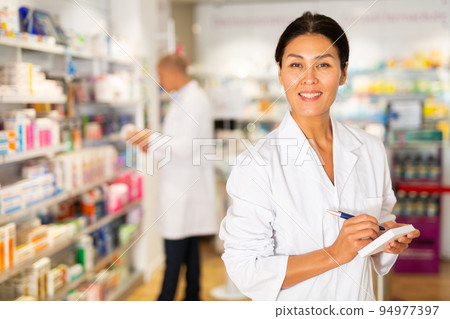 Positive female pharmacist writes in a notebook in the trading floor of pharmacy Positive female pharmacist writes in a notebook in the trading floor of pharmacy 94977397