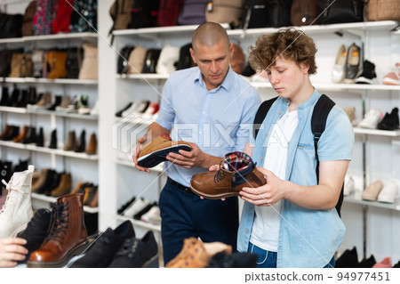 Man and teenage boy choosing demi-season shoes in store 94977451